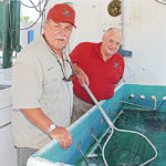 Sid Bourgeois dips live bait for a customer as his father and business partner Joe looks on.