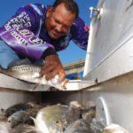 Against a blue October sky, Capt. Eric Dumas stuffs another speckled trout into his already amply filled ice box.