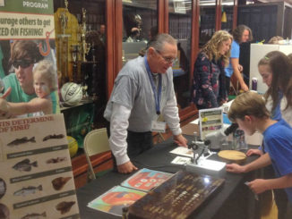 A volunteer instructor teaching about the growth of fish and how scientists determine their age just from a tiny ear bone.